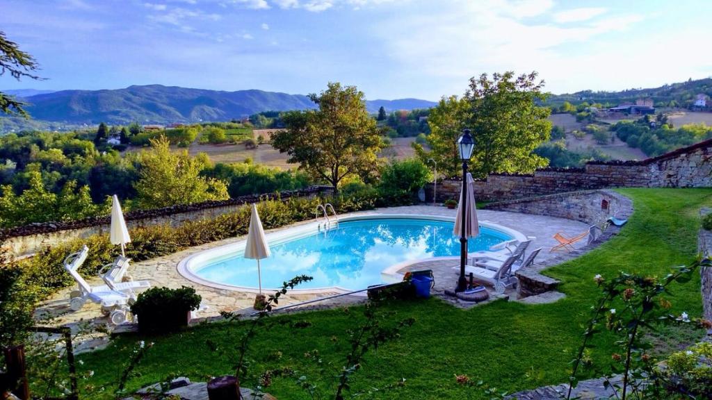 a swimming pool in a yard with chairs and umbrellas at Castello di Grillano Guest House in Ovada