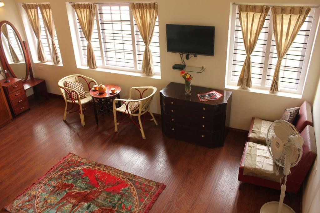 ein Wohnzimmer mit einem Tisch, Stühlen und einem TV in der Unterkunft Colonels inn in Udagamandalam
