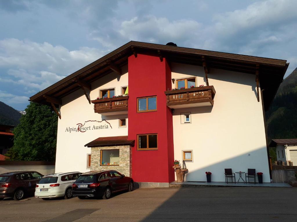 ein rotweißes Gebäude mit Autos auf einem Parkplatz in der Unterkunft Alpin Resort Austria in Bichlbach