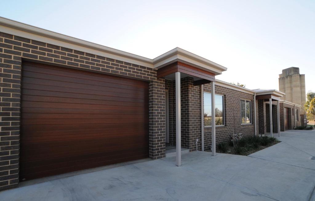 a brick house with a wooden garage door at Doze On Green in Wangaratta
