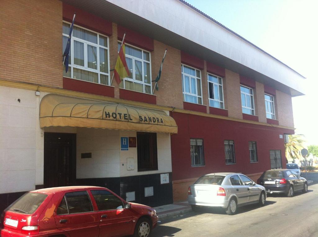 a red building with cars parked in front of it at Hotel Sandra in Alcalá de Guadaira