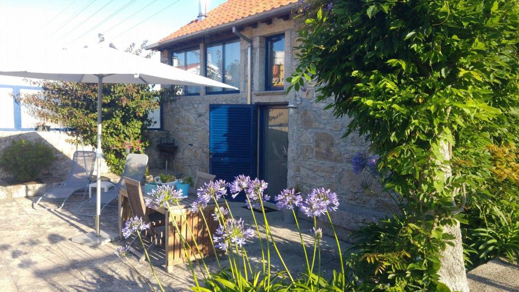 ein Haus mit einem Tisch, einem Regenschirm und lila Blumen in der Unterkunft Casinha Nº461 in Vila Praia de Âncora