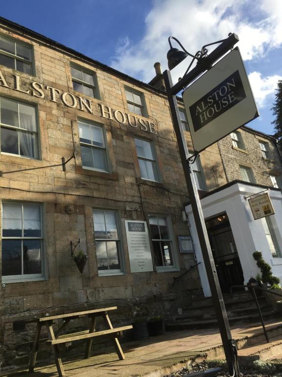 ein Schild vor einem Gebäude mit einer Holzbank in der Unterkunft Alston House Hotel in Alston