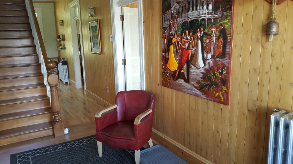 a red chair in a hallway with a painting on the wall at Le Manoir du Vieux Presbytère in Port-Daniel
