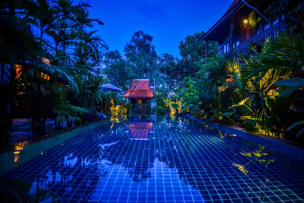 A resort pool glowing blue among tropical buildings after dark.