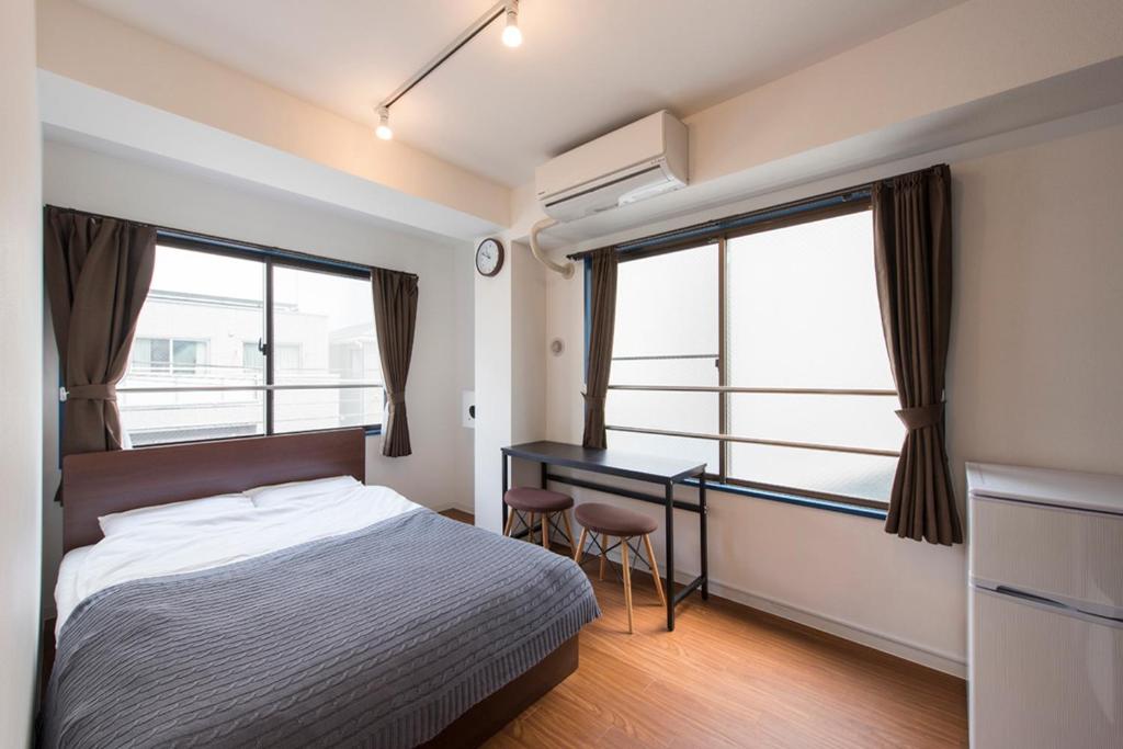 1 dormitorio con 1 cama, escritorio y ventanas en World Travelers Hostel UENO, en Tokio