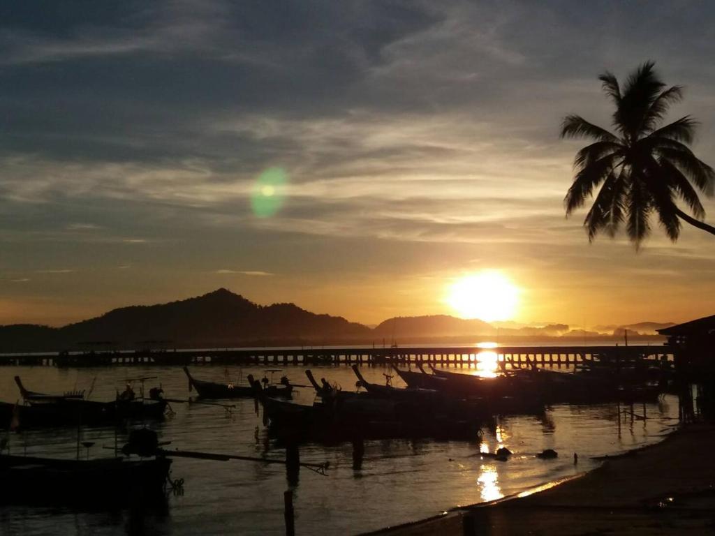 um pôr do sol com uma palmeira e barcos na água em Seaside home em Ko Mook