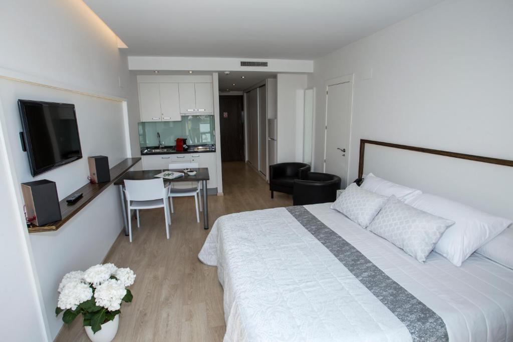 a bedroom with a large white bed and a kitchen at ApartHotel Playa Oliva in Oliva