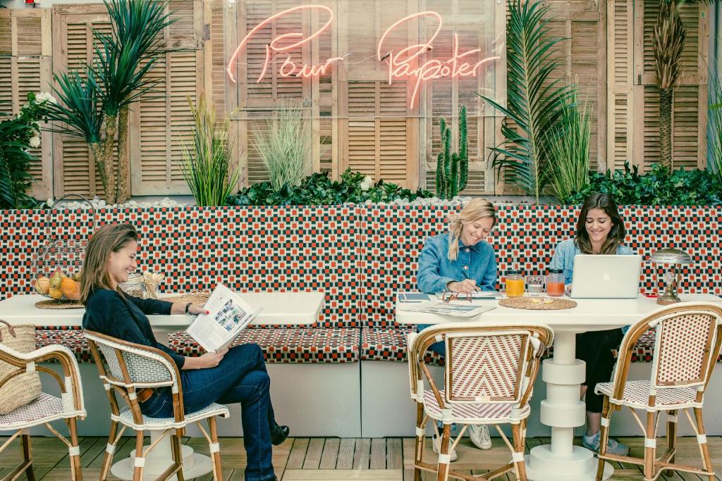 drei Frauen sitzen an Tischen in einem Restaurant mit Laptops in der Unterkunft Bob Hotel in Paris