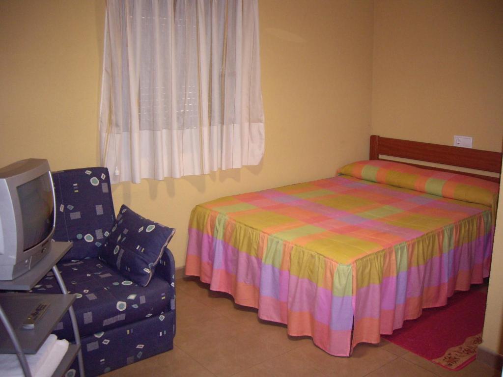 a bedroom with a bed and a chair and a tv at Pensión la Estación in Nubledo