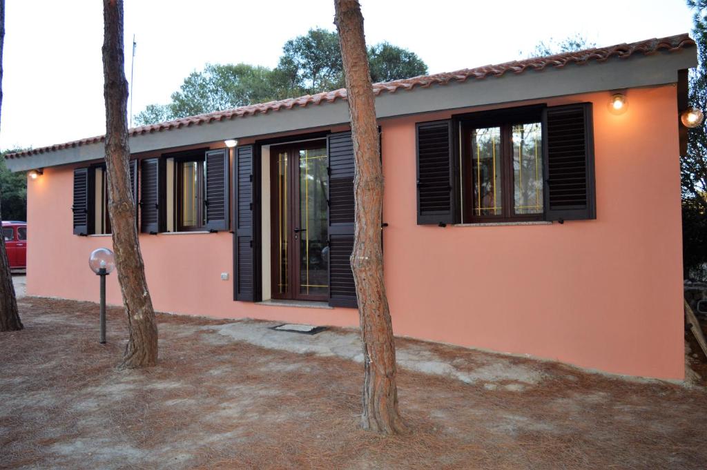 ein rosafarbenes Haus mit schwarzen Fenstern und Bäumen in der Unterkunft Pineta Spiaggia Grande 2 in SantʼAntìoco
