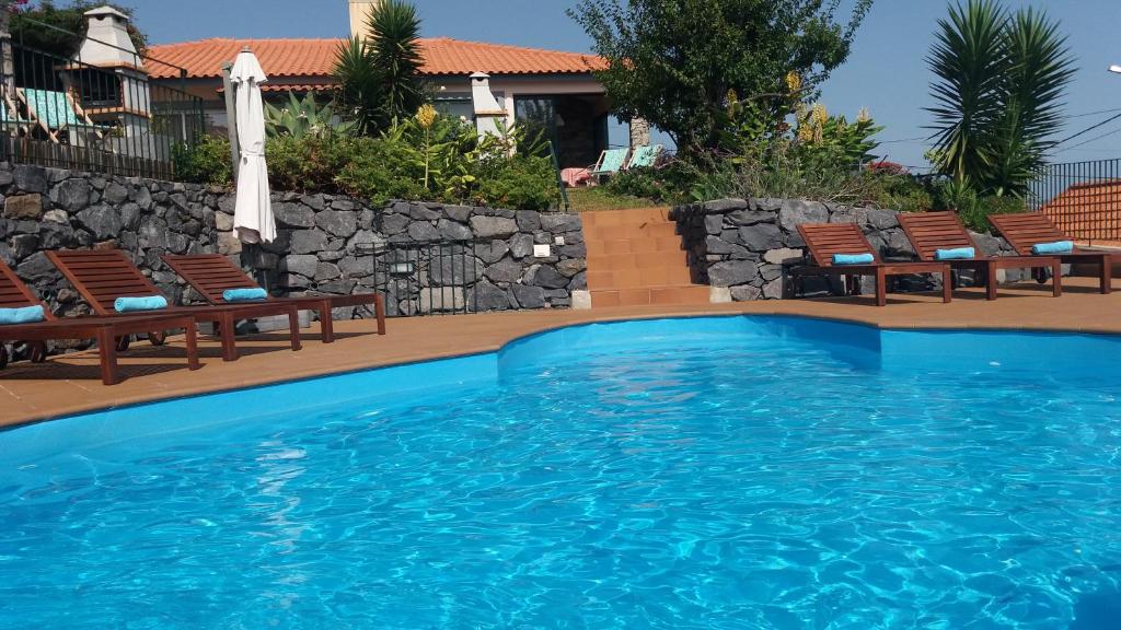 a swimming pool with chairs and an umbrella at Banda Do Sol Self Catering Cottages in Estreito da Calheta