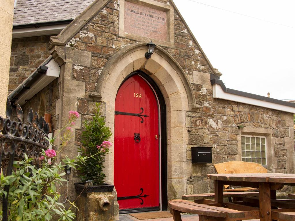 czerwone drzwi w kamiennym budynku z ławką w obiekcie James John Hamilton House and backpacker hostel w mieście Fishguard