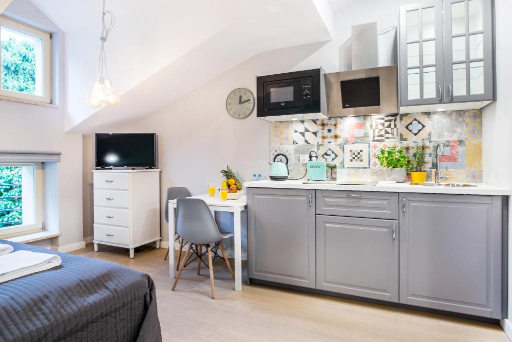 Compact kitchenette with gray cabinets, dining table, TV and patterned tile backsplash.