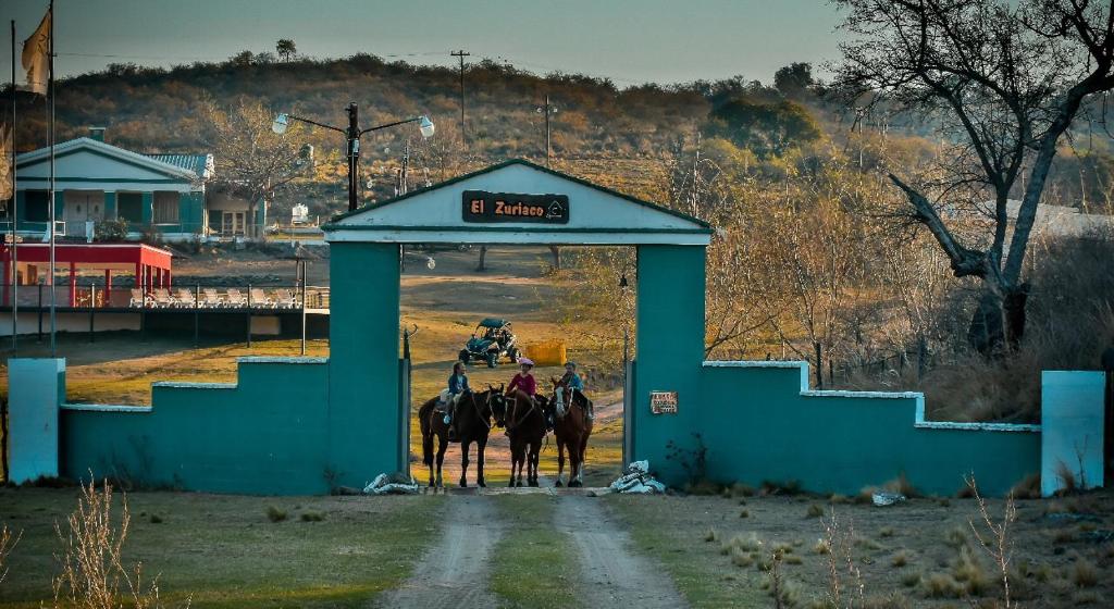 a group of people riding horses through a gate at El Zuriaco in Santa Rosa de Calamuchita
