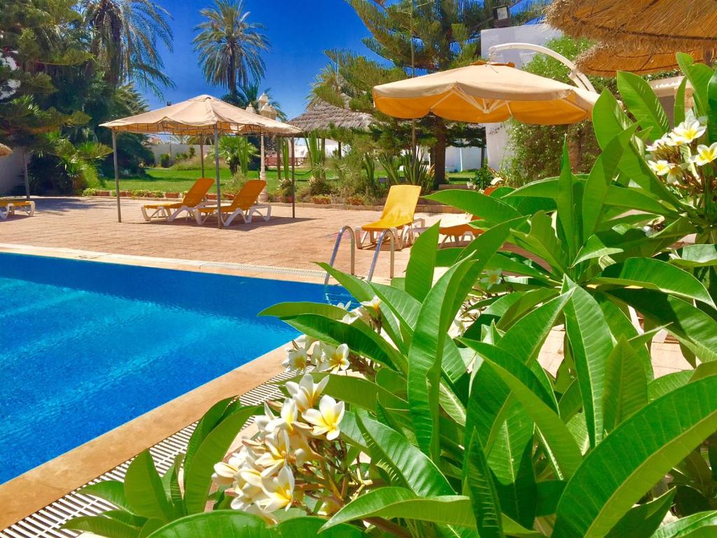 einen Pool mit Stühlen und Sonnenschirmen neben einem Resort in der Unterkunft Hotel Djerba Orient in Mezraya