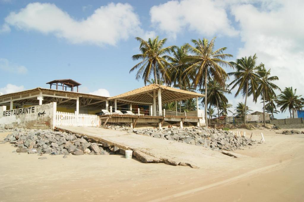 a building on the beach with rocks and palm trees at Pousada Corais de Maracajaú in Maracajaú