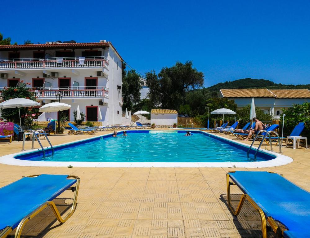 uma grande piscina com cadeiras azuis e um edifício em Hotel Olga em Agios Stefanos