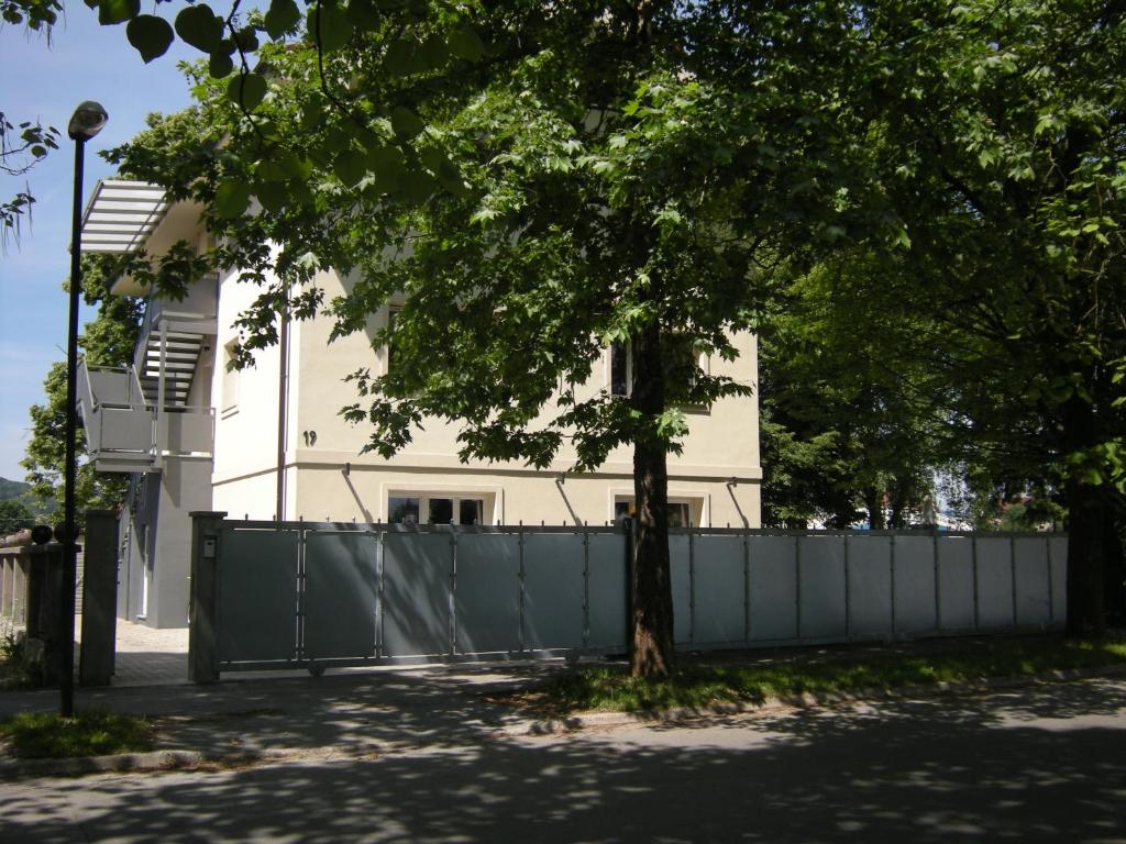 un bâtiment blanc avec une clôture et un arbre dans l'établissement Vila Ema Apartments and Rooms, à Ljubljana