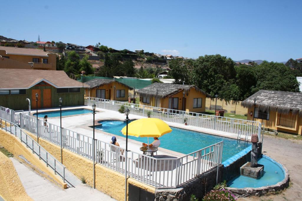 a swimming pool with a yellow umbrella and some houses at Apart Hotel Escala Real in Coquimbo