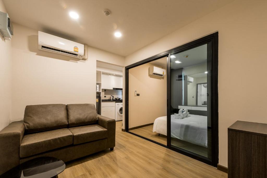 A living room with a sofa facing a media wall and a glass-partitioned bedroom.