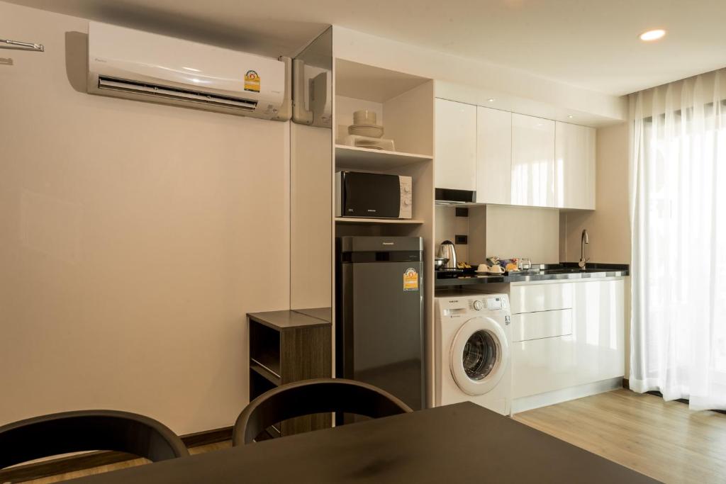 A compact apartment kitchen with a refrigerator, washing machine, dining table, and bright window.