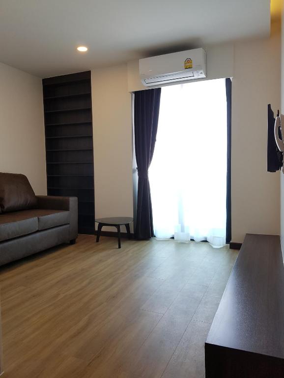 A spacious living area with a sofa, shelving, console, and tall curtained window.