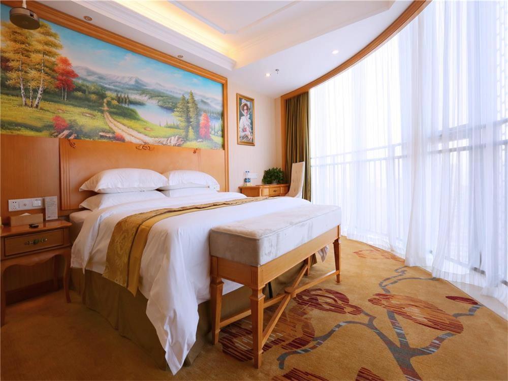 a bedroom with a large bed with a painting on the wall at Vienna International Hotel Yantai Changjiang Road Xingyi Square Branch in Yantai