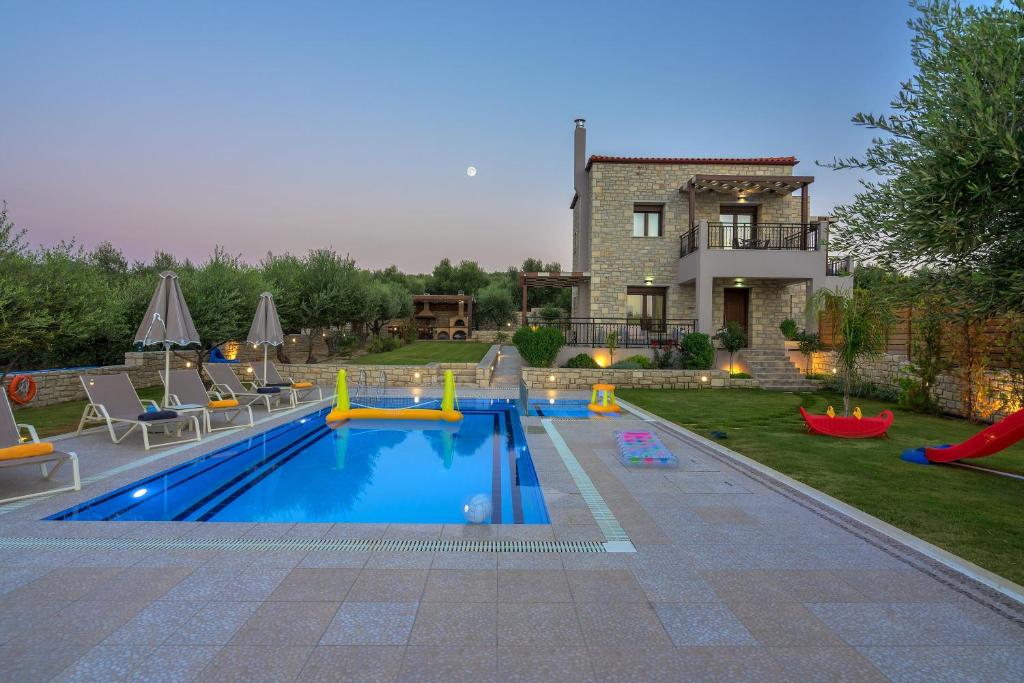 a swimming pool with a playground in front of a house at Olive Garden Villas in Perama