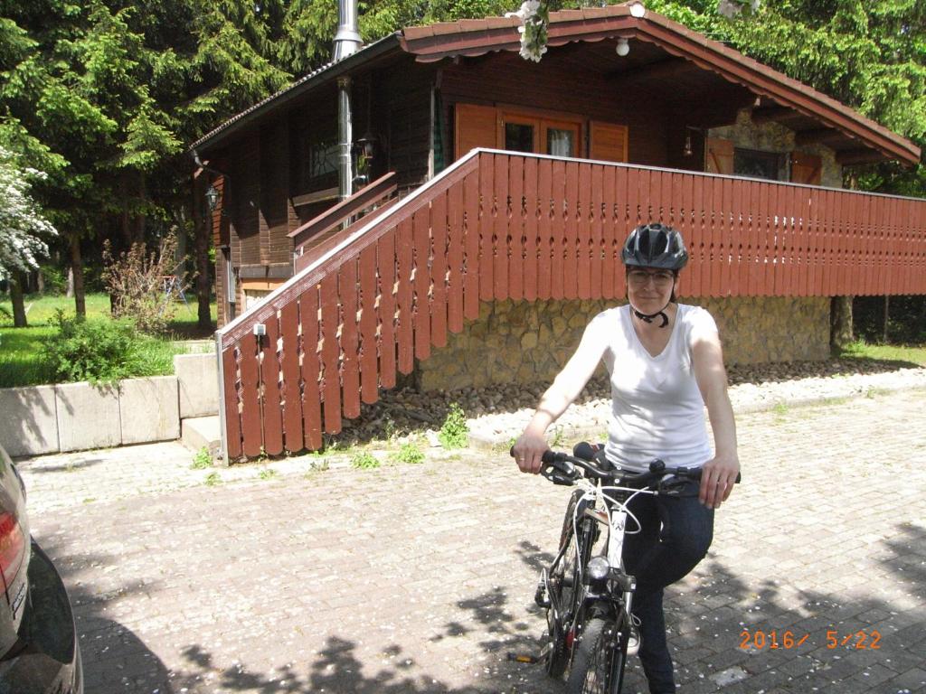 a woman riding a bike in front of a house at Grimm`s Waldhäuschen in Mudau