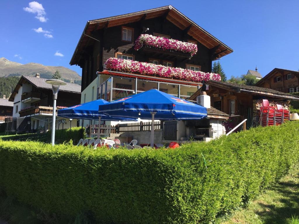 ein Haus mit einem blauen Regenschirm und einem Gebäude mit Blumen in der Unterkunft Hotel Haus Mühlebach in Ernen