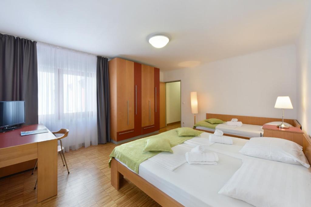 a bedroom with two beds and a desk and a television at Hotel Korotan in Vienna