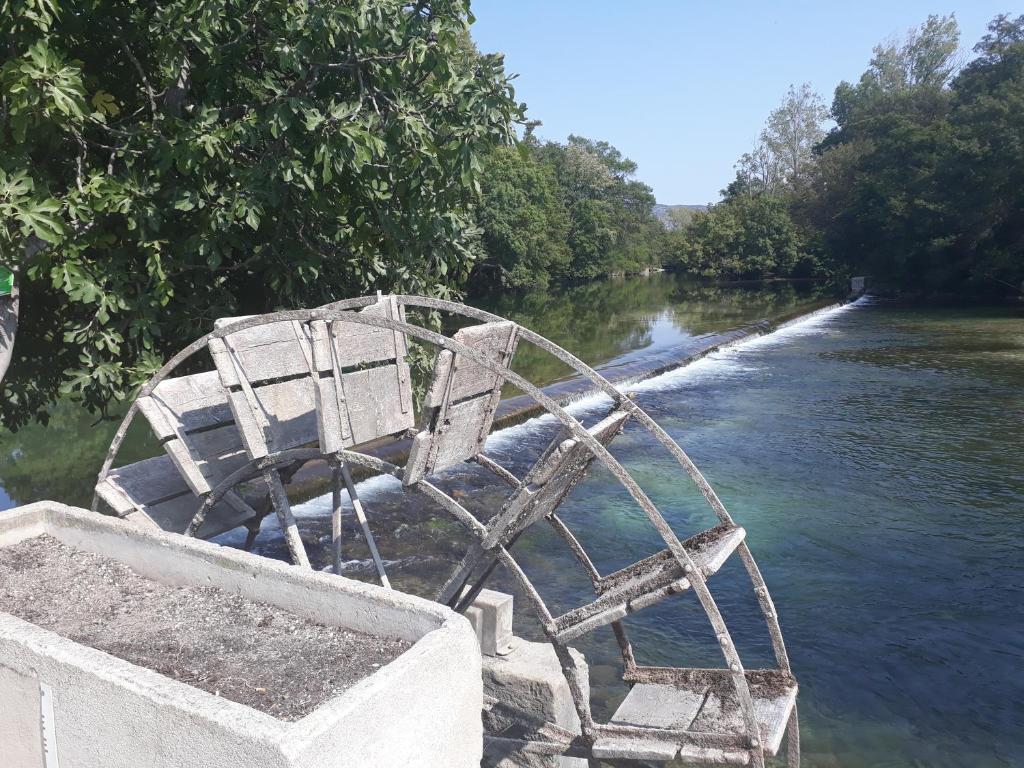 a bench sitting on the side of a river at Mas et Gite de la Picholine in LʼIsle-sur-la-Sorgue