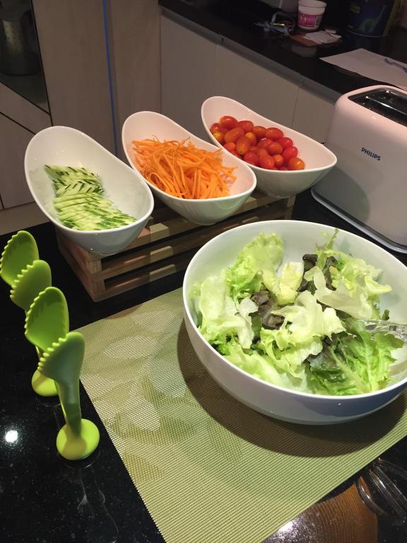 A self-serve salad station with bowls of cucumber, carrot, tomato and lettuce.