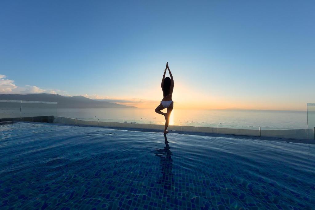 Eine Frau, die Yoga am Rande eines Pools macht. in der Unterkunft Belle Maison Parosand Da Nang Hotel -managed by H&K Hospitality in Đà Nẵng