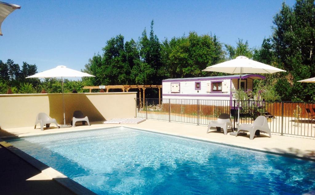 une piscine avec des chaises et des parasols ainsi qu'une maison dans l'établissement Des roulottes en Provence, à Barbentane