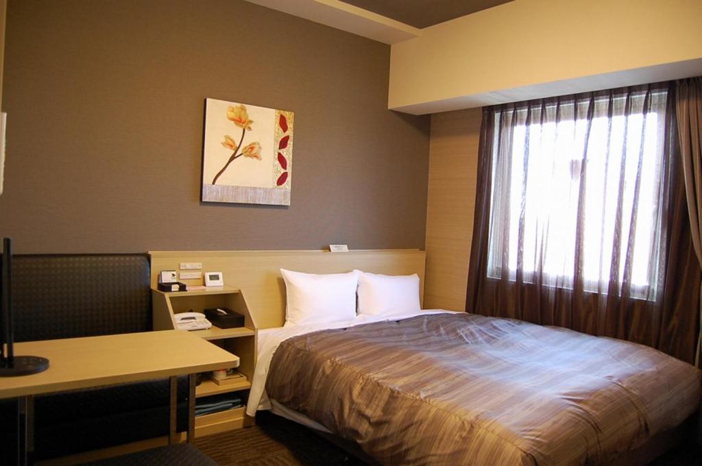 a hotel room with a bed and a desk and a window at Hotel Route Inn Toyota Motomachi in Toyota