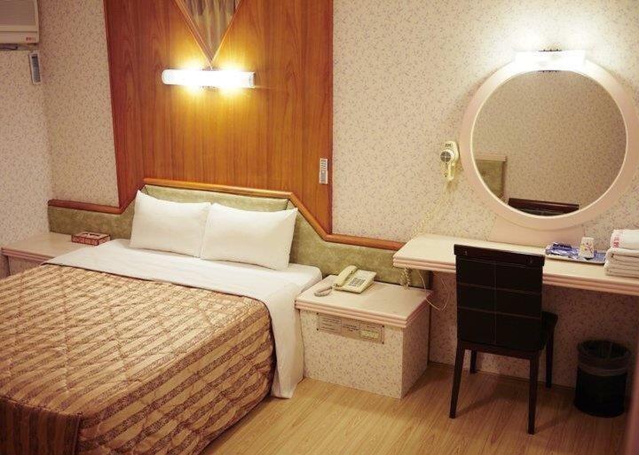 um quarto de hotel com uma cama e um espelho em Green Yard Business Hotel em Miaoli