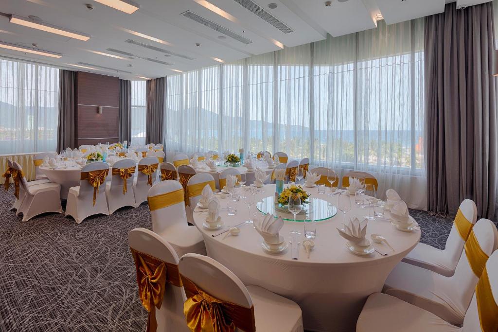 einen Konferenzraum mit weißen Tischen und Stühlen sowie großen Fenstern in der Unterkunft Belle Maison Parosand Da Nang Hotel -managed by H&K Hospitality in Đà Nẵng