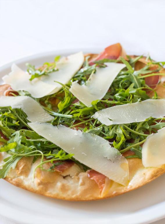 a pizza with greens and cheese on a white plate at Thirides Beach Resort in Gythio