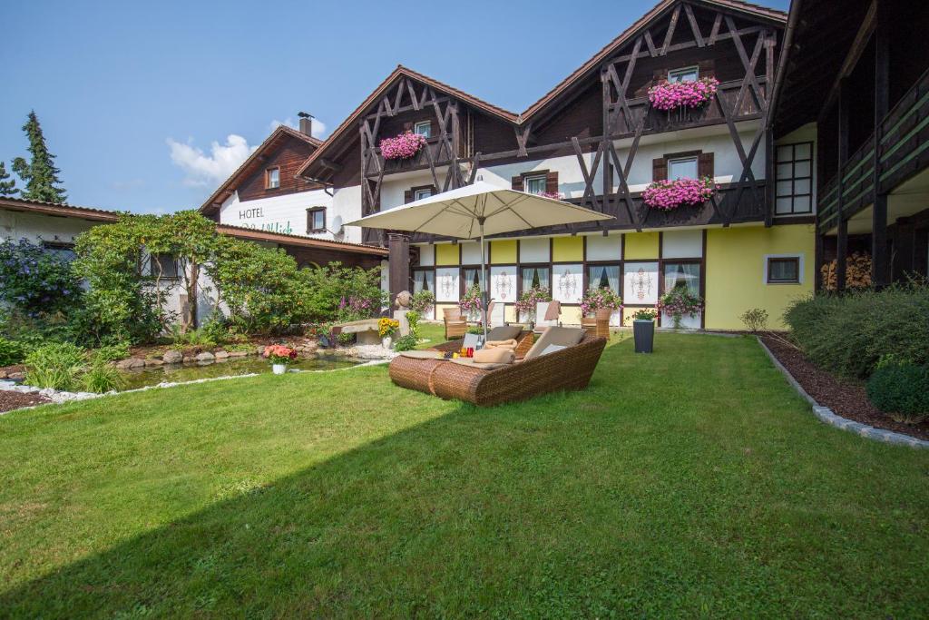 a house with a lawn with a couch and an umbrella at Hotel Waldblick in Bodenmais