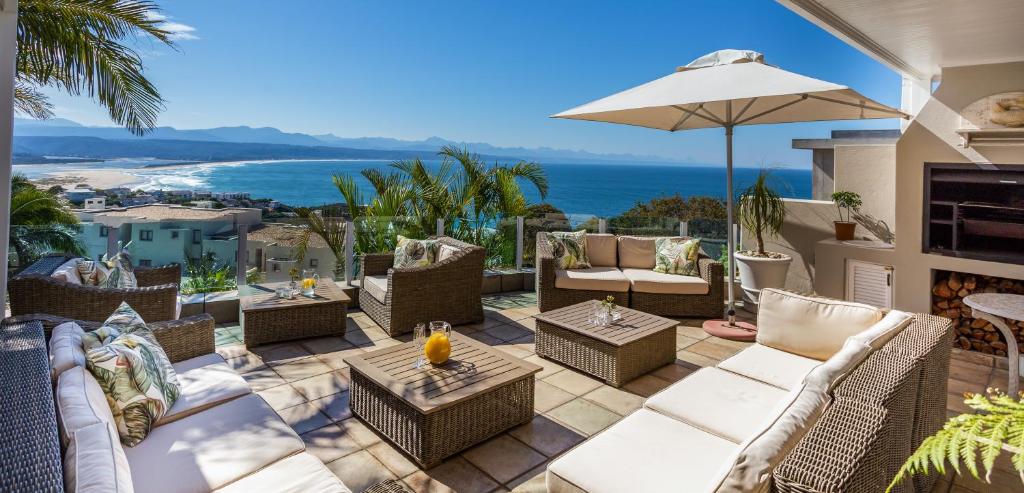 eine Terrasse mit Stühlen, Tischen und einem Sonnenschirm in der Unterkunft Ocean Watch Guest House in Plettenberg Bay