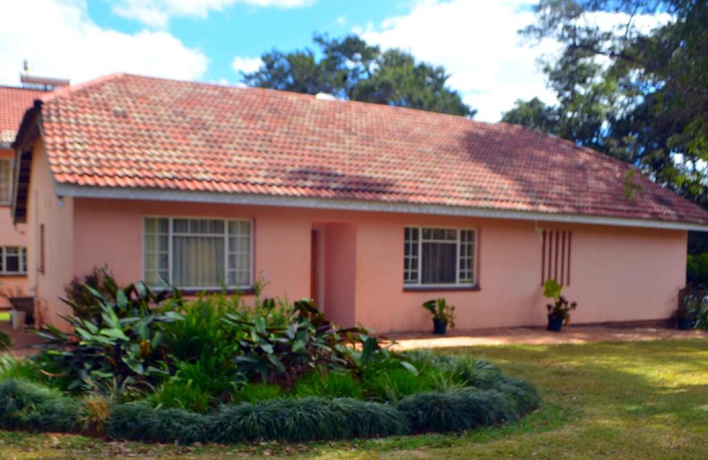 una casa rosa con techo rojo en Tinotenda Cottage en Harare