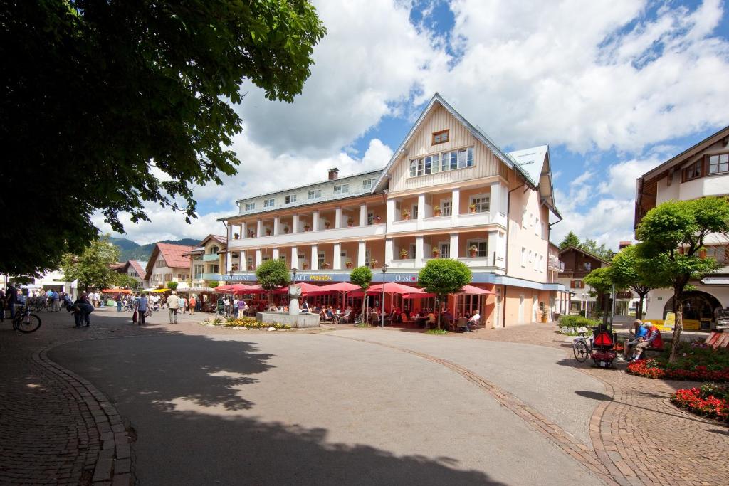 een groot wit gebouw met rode parasols op een straat bij Hotel Mohren in Oberstdorf