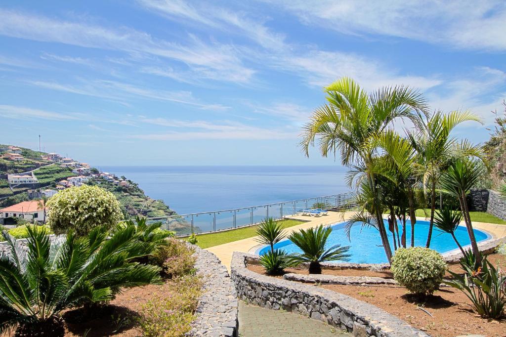 a swimming pool with palm trees and the ocean at Peace Haven in Calheta