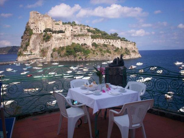 una mesa y sillas en un balcón con un castillo en Hotel Villa Antonio en Ischia
