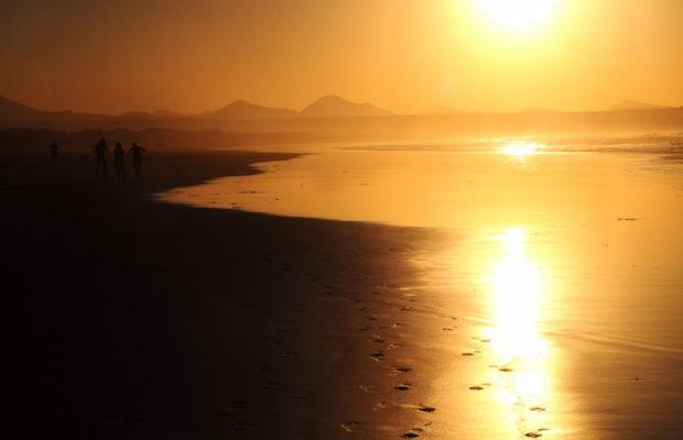 a group of people walking on the beach at sunset at Blue Beach in Famara