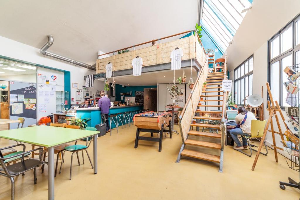 a room with people sitting at tables and a staircase at Alter'hostel in Lyon