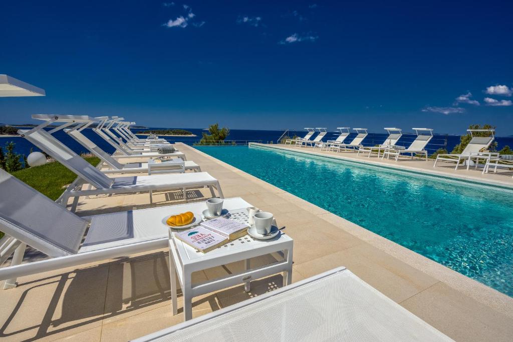 a row of chairs and a swimming pool with the ocean at Golden Rays Luxury Villas & Apartments in Primošten