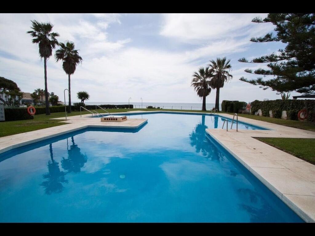 a large blue swimming pool with palm trees and the ocean at apartment by the beach in Mijas Costa